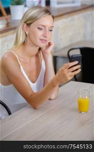 young woman texting in a bar with an orange juice