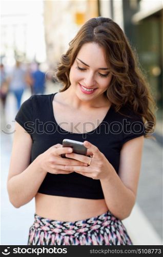 Young woman texting with a smartphone in urban background. Girl wearing spring clothes