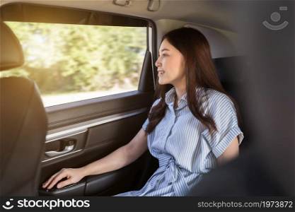 young woman thinking and looking view out of window while sitting in the back seat of car