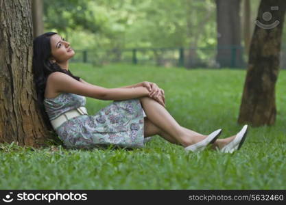 Young woman thinking while leaning against a tree