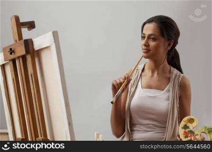 Young woman thinking while painting on canvas