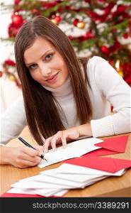 Young woman thinking while writing Christmas card in front of tree