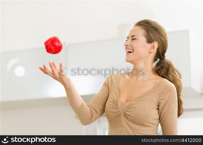 Young woman throwing apple in kitchen