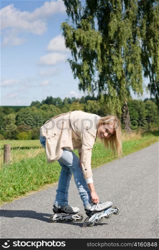 Young woman tightening inline skates on sunny asphalt road
