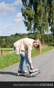 Young woman tightening inline skates on sunny asphalt road