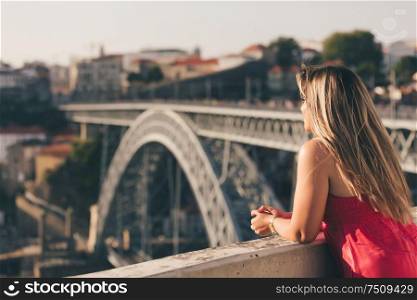 Young woman tourist enjoying beautiful landscape view on the old town with river and famous iron bridge during the sunset in Porto city, Portugal
