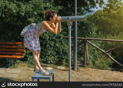 Young woman tourist in summer dress using monocular telescope binoculars to watch the scene from the mountain at the Aristotle&rsquo;s park at Stagira Greece in autumn