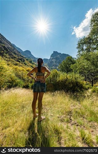 Young woman tourist looking to the top of mountain on a sunny bright day. Active female tourist at incredibly beautiful landscape. On background forest.