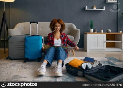 Young woman tourist reading travel map surrounded with packed luggage. Vacation planning. Woman reading travel map surrounded with luggage