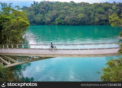 Young woman tourists riding bicycle across the white bridge at Sun moon lake in Nantou, Taiwan