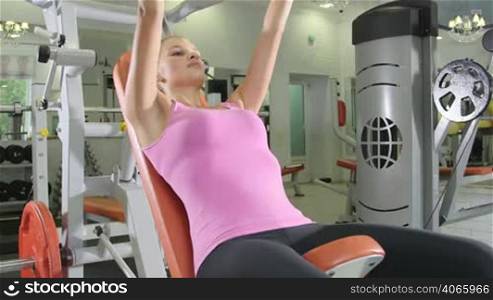 Young woman training in free weights area at health fitness club on chest press machine jib crane shot