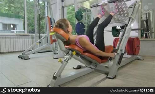Young woman training in health fitness club using exercise machine for leg muscles jib crane shot
