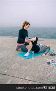 Young woman training senior woman by sea pier. Female trainer with senior woman