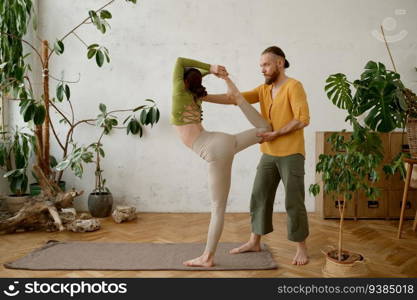 Young woman training yoga with male instructor indoors. Man teacher helping female student to make Trikonsana asana. Young woman training yoga with male instructor indoors