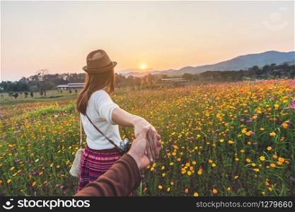 Young woman traveler holding man&rsquo;s hand and leading him on flowers field, Couple vacation travel concept