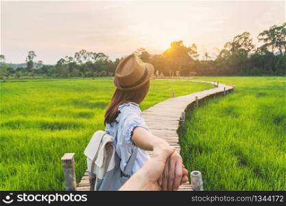 Young woman traveler holding man&rsquo;s hand and leading him on green paddy field, Couple vacation travel concept