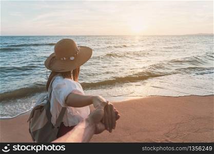 Young woman traveler holding man&rsquo;s hand and looking beautiful sunset on the beach, Couple vacation travel summer concept