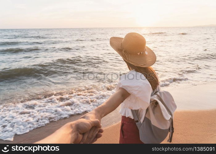 Young woman traveler holding man&rsquo;s hand and looking beautiful sunset on the beach, Couple vacation travel summer concept