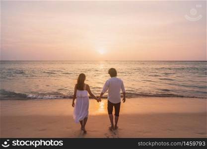 Young woman traveler holding man&rsquo;s hand and looking beautiful sunset on the beach, Couple on vacation in summer concept