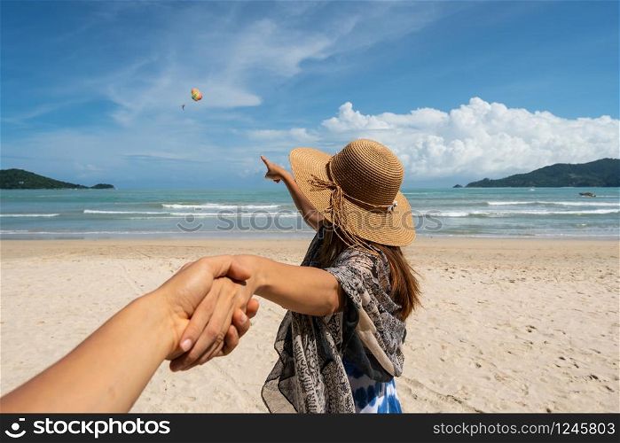 Young woman traveler holding man&rsquo;s hand and looking parachute flying in the sky on the beach, Couple vacation travel summer concept. Young woman traveler holding man&rsquo;s hand and looking parachute flying in the sky on the beach
