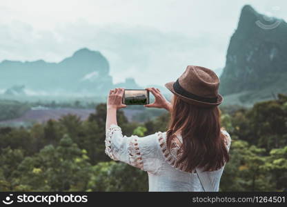 Young woman traveler looking and taking a photo with smartphone at beautiful view