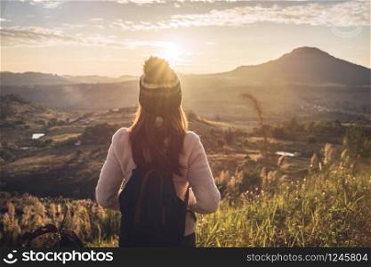 Young woman traveler looking at sunrise over the mountain with sunlight and flare. Cheering young woman traveler looking at sunrise