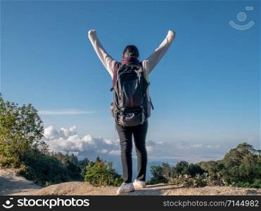 Young woman traveler raise arms to show success at peak of mountains on summer vacations day. Lifestyle hiking concept.