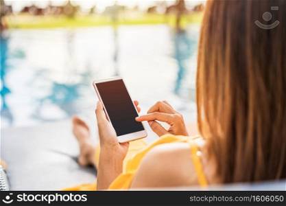 Young woman traveler relaxing and using a mobile phone by a hotel pool while traveling for summer vacation