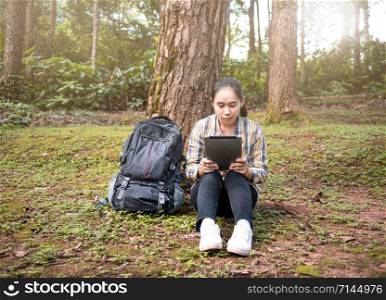 Young woman traveler searches GPS coordinates by tablet PC at nature trail in summer vacations day. Technology and Travel concept.
