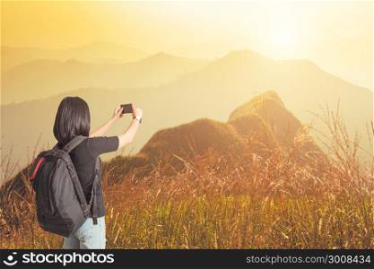 Young woman traveler taking photo of mountains in sunset.Life and lifestyle concept. Vacation and long weekend.