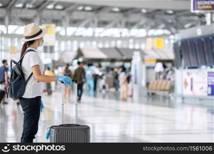 Young woman traveler wearing face mask and nitrile glove holding handle luggage in airport terminal, protection Coronavirus disease (Covid-19) infection. New Normal and travel bubble concept