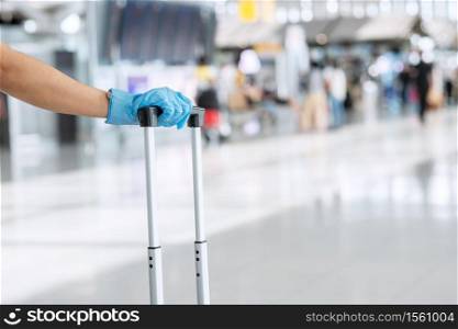 Young woman traveler wearing nitrile glove holding handle luggage in airport terminal, protection Coronavirus disease (Covid-19) infection. New Normal and travel bubble concept