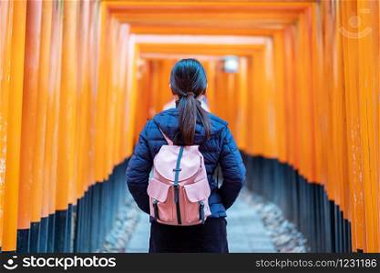 Young woman traveling at Fushimi Inari taisha Shrine, happy asian traveler looking vibrant orange torii gates. landmark and popular for tourists attractions in Kyoto, Japan. Asia travel concept