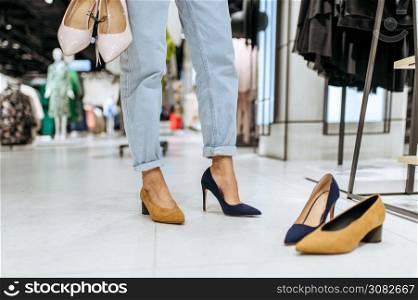 Young woman trying on shoes in clothing store, view on feets. Female person shopping in fashion boutique, shopaholic, shopper looking on boots. Woman trying on shoes in store, view on feets