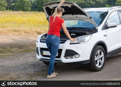 Young woman trying to repair brokedown car at countryside