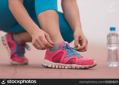 Young woman tying shoelaces on sneakers on a promenade. Standing next to a bottle of water. Exercise outdoors