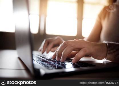 Young Woman Typing Computer Laptop Keyboard. Closeup shot and Selective focus on Finger. Working on Desk against Window