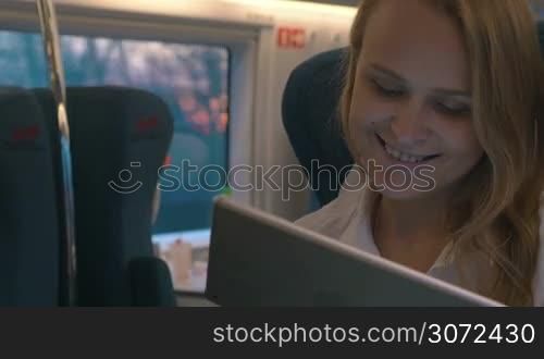Young woman typing message on digital tablet with thoughtful look while traveling by express train