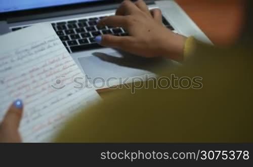 Young woman typing on laptop computer keyboard for homework. Hispanic girl and college education. Female student studying and using pc at home. Over the shoulder shot