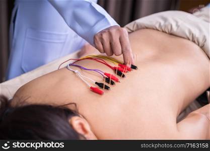 young woman undergoing acupuncture treatment with electrical stimulator on back