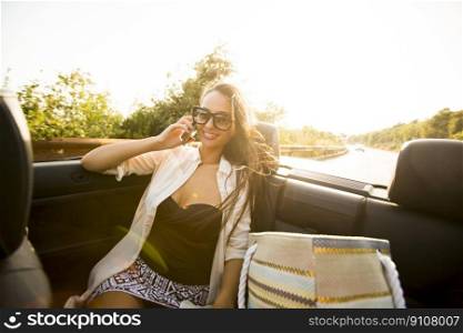 Young woman uses  mobile phone and sitting in cabriolet at summer day