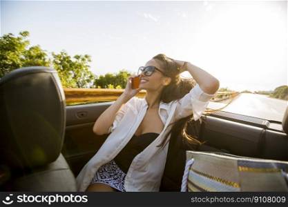 Young woman uses mobile phone and sitting in cabriolet at summer day