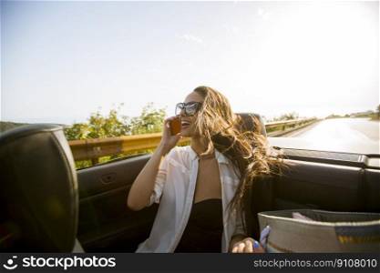 Young woman uses mobile phone and sitting in cabriolet at summer day