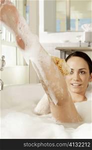 Young woman using a bath sponge on her leg