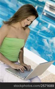 Young woman using a laptop at the poolside