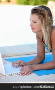 Young woman using a laptop by a swimming pool