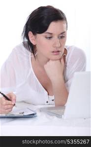 Young woman using a laptop computer and a pen and paper