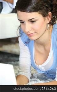 Young woman using a laptop lying on a rug