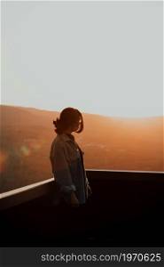 Young woman using a mask looking the mountains from a balcony during a super colorful sunset with copy space, freedom and wellness concept