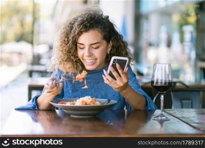 Young woman using a mobile phone while having lunch at a restaurant.